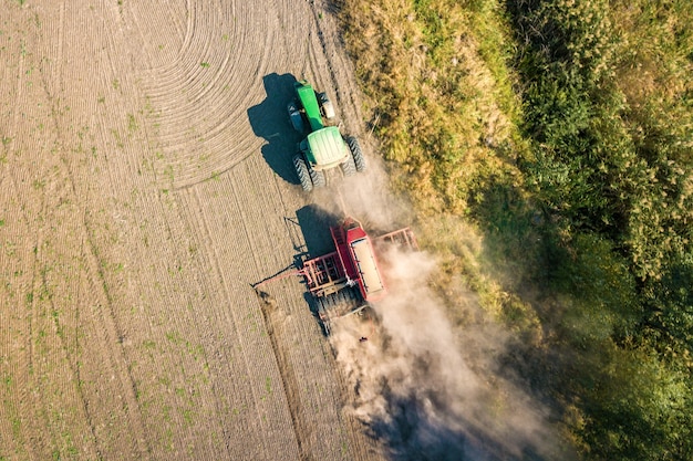 Vista aerea dall'alto verso il basso del trattore verde che coltiva il terreno e semina un campo asciutto