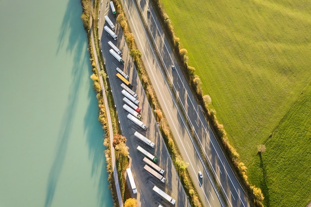 Vista aerea dall'alto verso il basso della strada da uno stato all'altro dell'autostrada con traffico rapido e parcheggio con i camion parcheggiati.