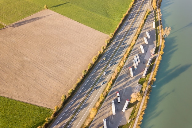 Vista aerea dall'alto verso il basso della strada da uno stato all'altro dell'autostrada con traffico rapido e parcheggio con i camion parcheggiati.