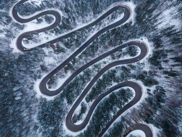 Vista aerea dall'alto verso il basso della strada tortuosa invernale nella foresta Transilvania Romania