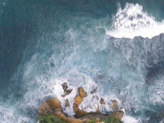 Vista aerea dall'alto verso il basso delle onde oceaniche giganti che si infrangono e si schiumeggiano nella spiaggia di corallo