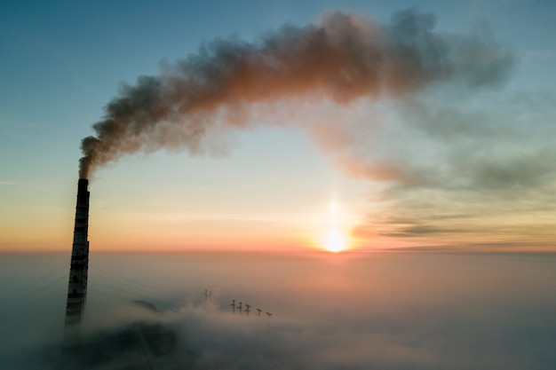 Vista aerea dei tubi alti della centrale elettrica del carbone con fumo nero che si alza atmosfera inquinante al tramonto.