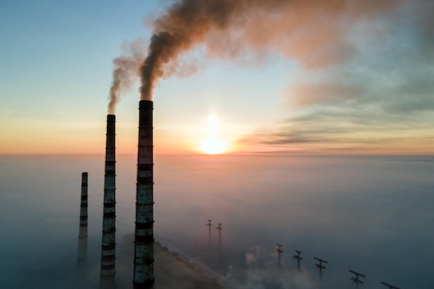 Vista aerea dei tubi alti della centrale elettrica del carbone con fumo nero che si alza atmosfera inquinante al tramonto.