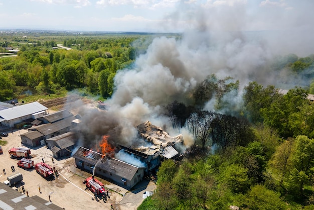 Vista aerea dei vigili del fuoco che estinguono l'edificio in rovina in fiamme con tetto crollato e fumo scuro in aumento.