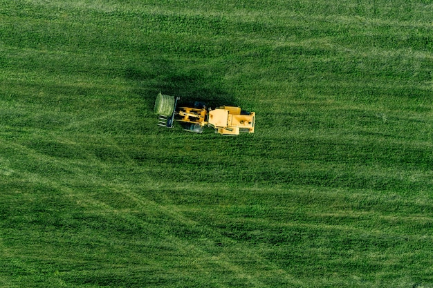 Vista aerea del campo di raccolta dell'erba verde con il trattore in movimento balla di fieno a Finalnd