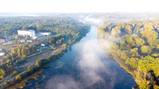 Vista aerea del drone che vola sopra il fiume con calma superficie dell'acqua riflettente e nebbia bianca e foschia