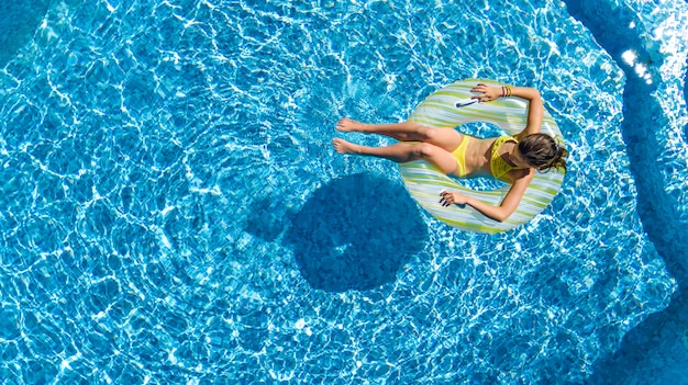 Vista aerea del drone della bambina nella piscina dall'alto, il bambino nuota sulla ciambella ad anello gonfiabile, il bambino si diverte in acqua blu sulla località di vacanza per famiglie