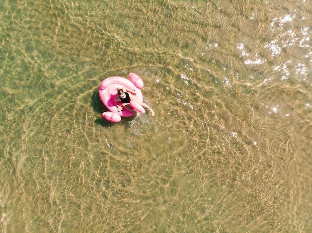 Vista aerea del drone della donna sul galleggiante della piscina di fenicotteri in mare