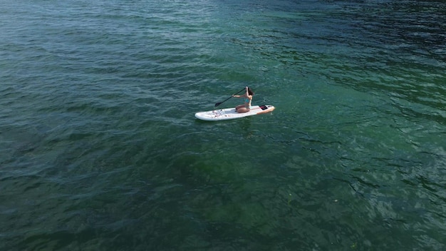 Vista aerea del drone di una giovane donna seduta su una tavola da paddle o sup in mare