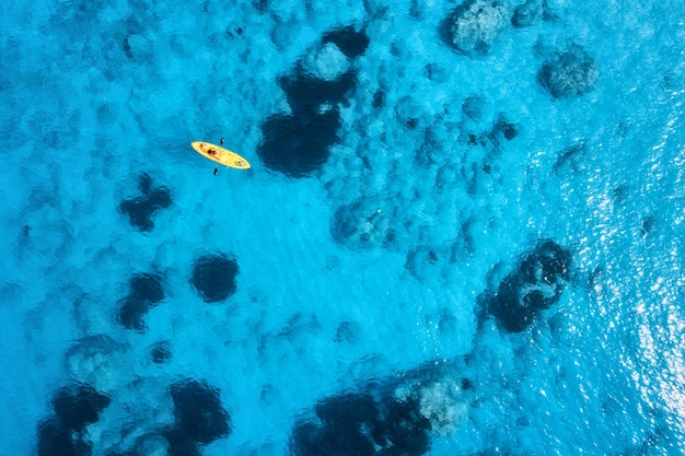 Vista aerea del kayak giallo nel mare blu al tramonto in estate Uomo su canoa galleggiante in acque azzurre chiare Isola di Lefkada Grecia Paesaggio tropicale Tavola Sup Viaggio attivo Vista dall'alto Vacanze