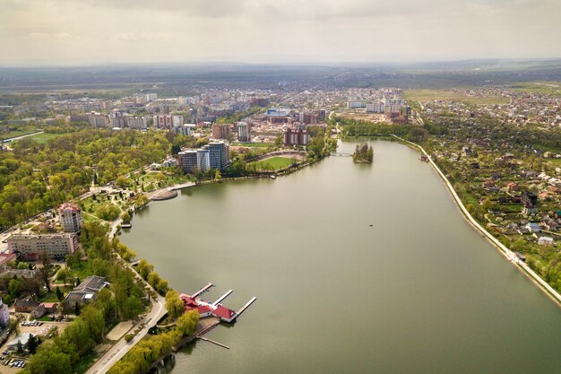 Vista aerea del lago della città fra gli alberi e le costruzioni verdi della città nella zona del parco di ricreazione. Fotografia di droni.