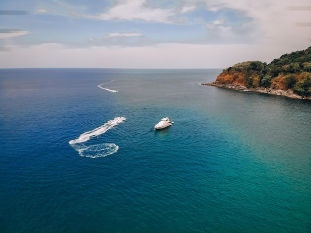 Vista aerea del motoscafo, lasciando traccia sulla superficie del mare blu vicino alla spiaggia verde; concetto di viaggio.