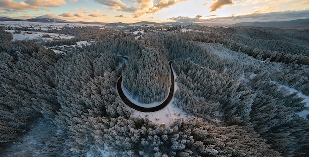 Vista aerea del paesaggio invernale con colline di montagna innevate e tortuosa strada forestale al mattino.
