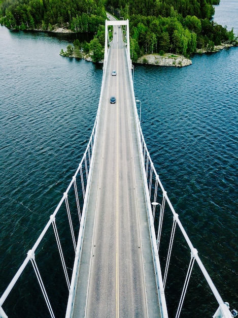 Vista aerea del ponte sospeso bianco con l'auto che attraversa il lago blu profondo nell'estate rurale della Finlandia