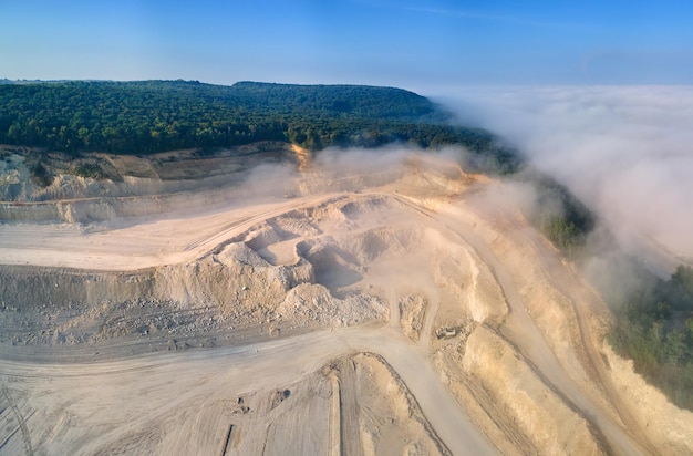 Vista aerea del sito minerario a cielo aperto di estrazione di materiali calcarei per l'edilizia con escavatori e autocarri con cassone ribaltabile.