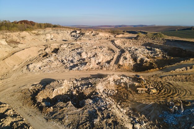 Vista aerea del sito minerario a cielo aperto di materiali calcarei per l'industria delle costruzioni con escavatori e autocarri con cassone ribaltabile