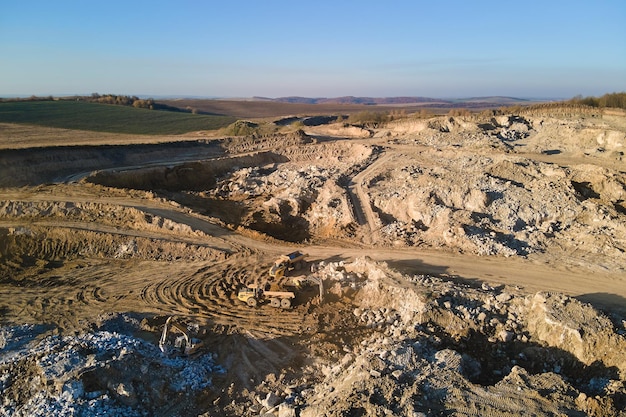 Vista aerea del sito minerario a cielo aperto di materiali calcarei per l'industria edile con escavatori e autocarri con cassone ribaltabile