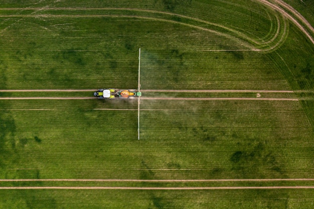 Vista aerea del trattore che spruzza i prodotti chimici sul grande campo verde