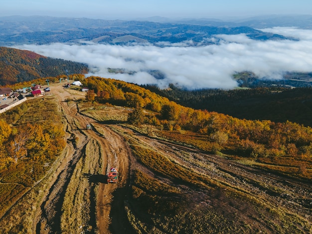 Vista aerea del viaggio fuoristrada suv salendo dalla collina di montagna copia spazio stagione autunnale sopra le nuvole