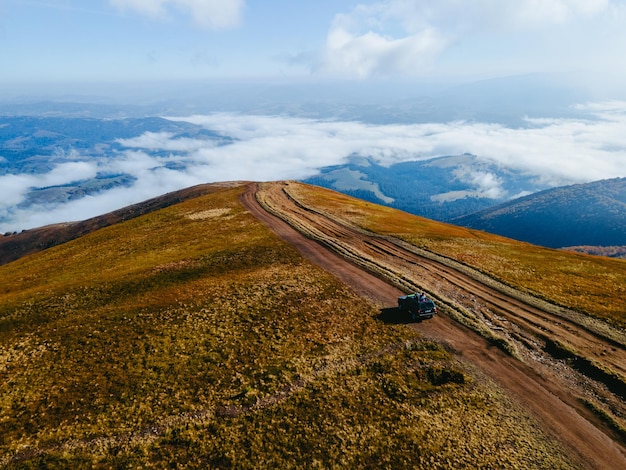 Vista aerea del viaggio fuoristrada suv salendo dalla collina di montagna copia spazio stagione autunnale sopra le nuvole