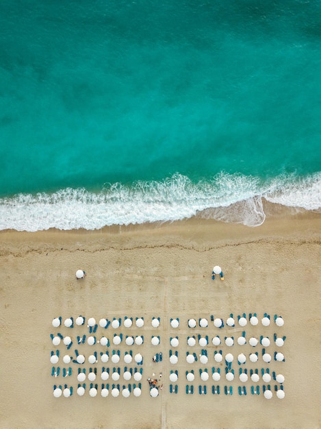 Vista aerea dell'incredibile spiaggia idilliaca vuota con ombrelloni bianchi e lettino blu.