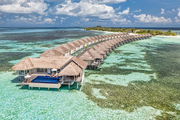 Vista aerea dell'isola delle Maldive, resort di ville sull'acqua di lusso e molo in legno. Bellissimo cielo e oceano