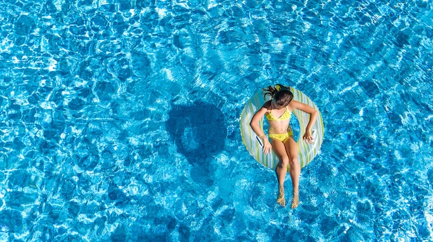 Vista aerea della bella ragazza in piscina dall'alto, nuotare sulla ciambella ad anello gonfiabile e si diverte in acqua in vacanza con la famiglia in vacanza tropicale