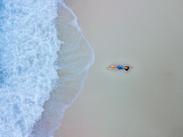 Vista aerea della donna in costume da bagno blu sulla spiaggia del mare