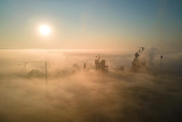 Vista aerea della fabbrica di cemento con struttura in calcestruzzo alta e gru a torre nel sito di produzione industriale in una mattinata nebbiosa Produzione e concetto di industria globale