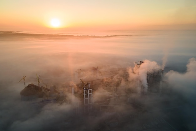 Vista aerea della fabbrica di cemento con struttura in calcestruzzo alta e gru a torre presso il sito di produzione industriale in serata nebbiosa Produzione e concetto di industria globale