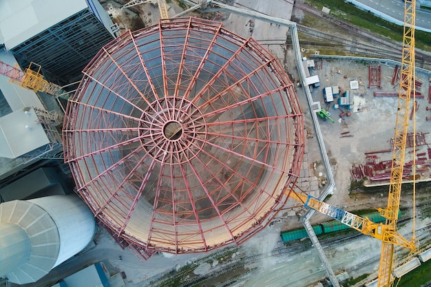 Vista aerea della fabbrica di cemento in costruzione con struttura dell'impianto in calcestruzzo alta e gru a torre nell'area di produzione industriale. Produzione e concetto di industria globale.