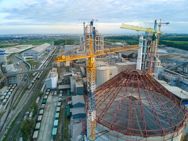 Vista aerea della fabbrica di cemento in costruzione con struttura in calcestruzzo alta e gru a torre nell'area di produzione industriale. Produzione e concetto di industria globale.