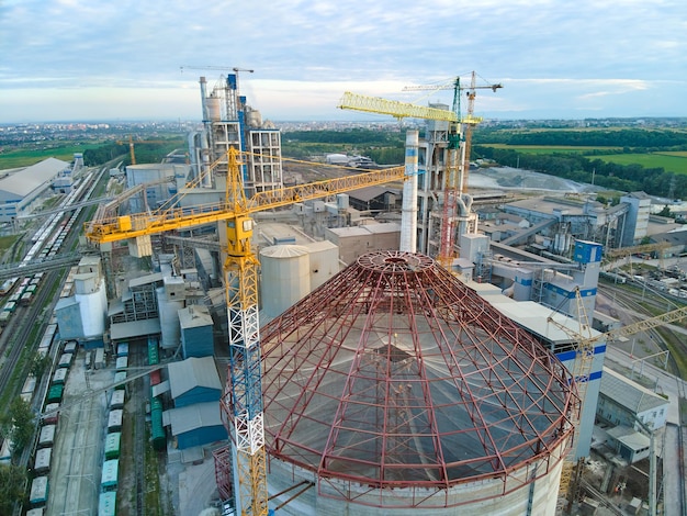 Vista aerea della fabbrica di cemento in costruzione con struttura in calcestruzzo alta e gru a torre nell'area di produzione industriale. Produzione e concetto di industria globale.