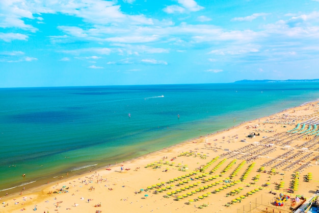 Vista aerea della spiaggia di Rimini con persone, navi e cielo blu,