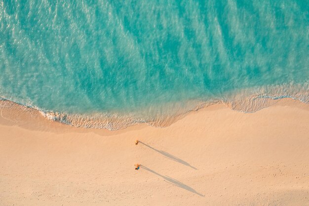 Vista aerea della splendida spiaggia con coppie che camminano nella luce del tramonto vicino al mare turchese. Vista dall'alto