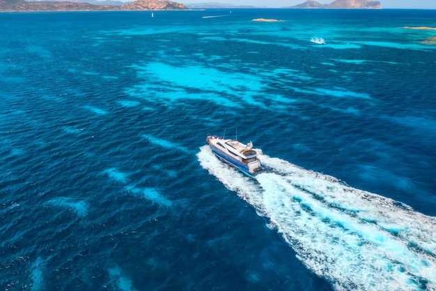 Vista aerea dello yacht galleggiante veloce sul mare blu in una giornata di sole in estate Viaggio in Sardegna Italia Vista aerea del motoscafo mare laguna acqua azzurra trasparente Vista dall'alto del drone Vista sul mare tropicale