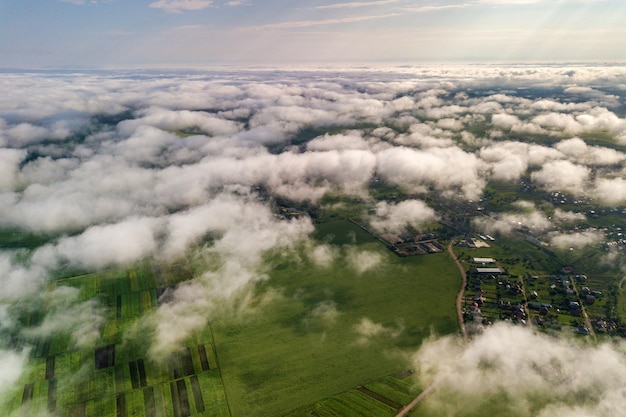 Vista aerea di nuvole bianche sopra una città o un villaggio con file di edifici e strade curve tra campi verdi in estate. Paesaggio di campagna dall'alto.