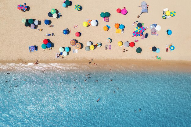 Vista aerea di ombrelloni colorati sulla spiaggia sabbiosa persone nel mare blu in una luminosa giornata di sole in estate Spiaggia Sardegna Italia Paesaggio tropicale con acqua turchese Viaggi e vacanze Vista dall'alto