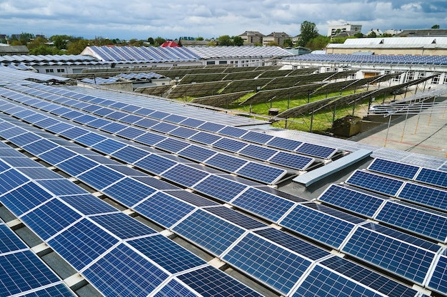 Vista aerea di pannelli solari fotovoltaici blu montati sul tetto di un edificio industriale per la produzione di elettricità ecologica verde. Concetto di produzione di energia sostenibile.