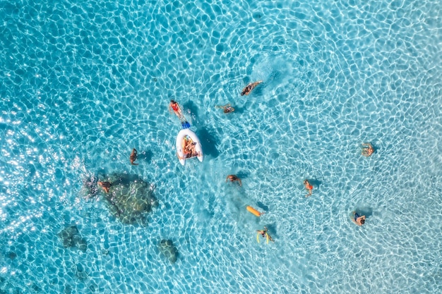 Vista aerea di persone felici che nuotano nel mare blu al tramonto in estate Vacanze in Sardegna Italia Vista dall'alto in basso di acque azzurre chiare spiaggia sabbiosa barca Paesaggio tropicale colorato Concetto di viaggio