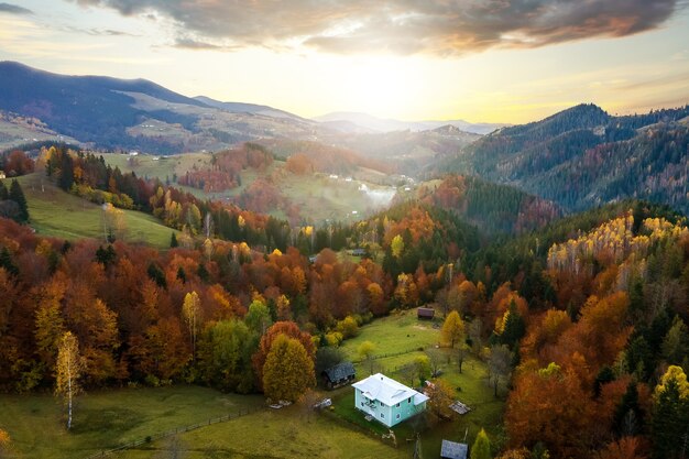 Vista aerea di piccole case di pastori su un ampio prato tra la foresta autunnale nelle montagne dei Carpazi ucraini al tramonto.