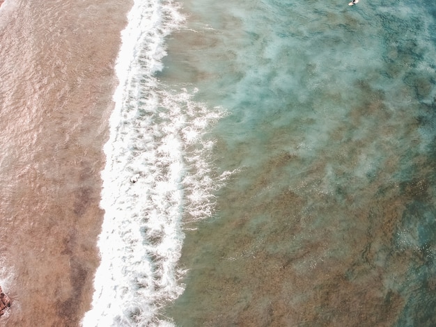 Vista aerea di surfisti tra le onde dell'Oceano Atlantico. Spiaggia di sabbia sullo sfondo