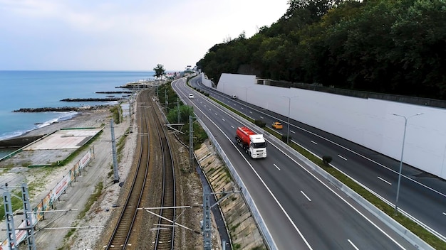 Vista aerea di un camion che guida su strada lungo la costa del mare e il concetto di trasporto su rotaia