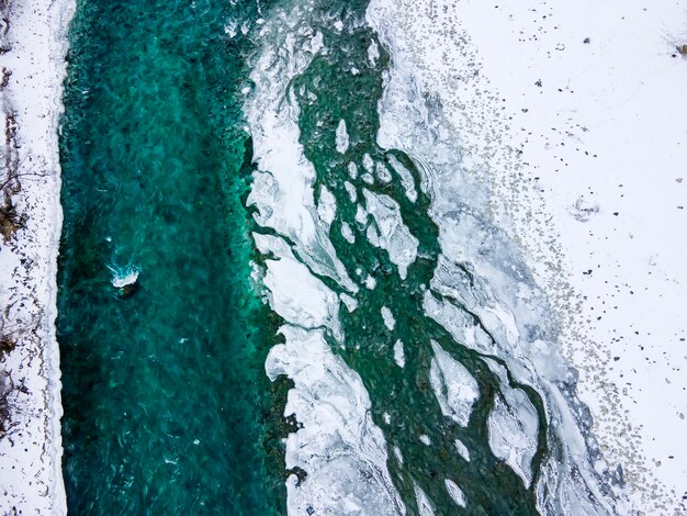 Vista aerea di un fiume blu e verde con neve e ghiaccio tritato durante una deriva di ghiaccio in inverno nelle montagne Altai in Russia.