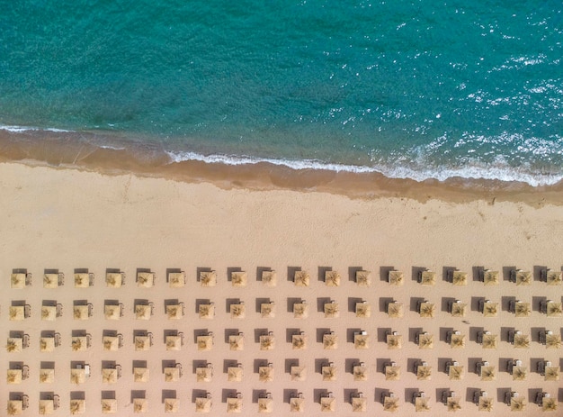 Vista aerea di un'incredibile spiaggia di sabbia vuota con ombrelloni di paglia e acque turchesi