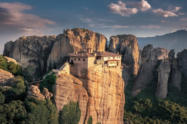 Vista aerea di un monastero ben illuminato in cima a una scogliera circondata da scogliere di montagna al tramonto