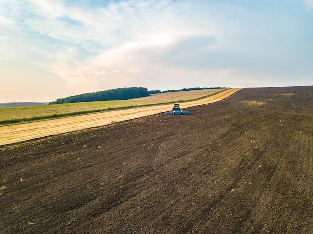 Vista aerea di un trattore che ara il campo nero dell'azienda agricola di agricoltura dopo la raccolta in autunno tardo.