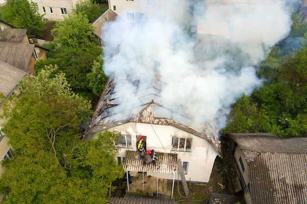 Vista aerea di una casa in fiamme con fiamme arancioni e fumo denso bianco.