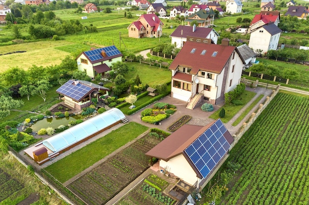 Vista aerea di una casa privata in estate con pannelli solari fotovoltaici blu sul tetto e cortile verde