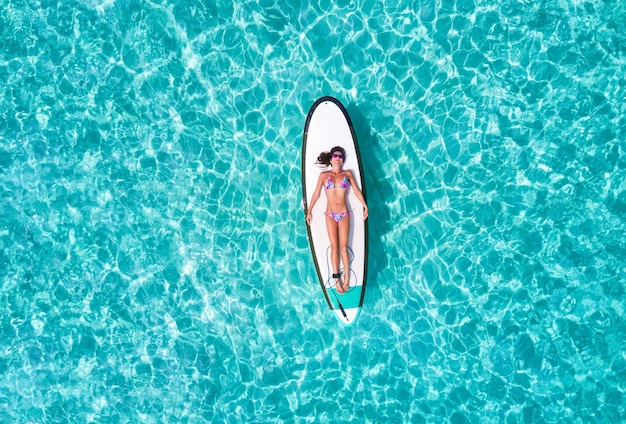 Vista aerea di una donna in bikini sdraiata su una tavola da surf sopra il mare